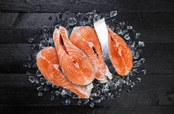 Filetes de salmón sobre hielo sobre mesa de madera negra vista superior — Foto de Stock