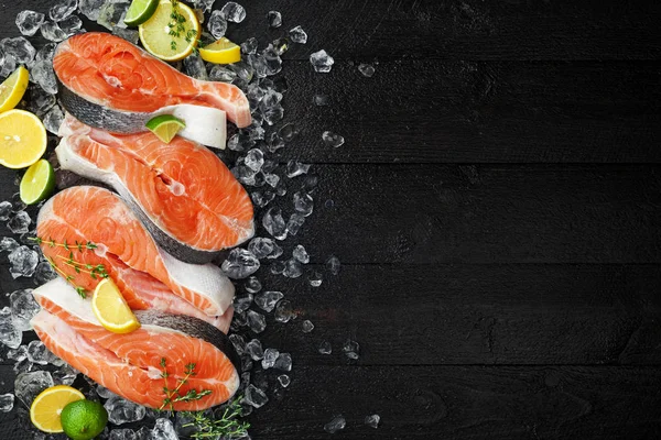 Filetes de salmón sobre hielo sobre mesa de madera negra vista superior. Concepto de comida para peces. Copiar espacio — Foto de Stock