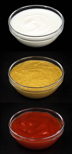 Кетчуп, майонез и горчица в стеклянных чашах изолированы на черном фоне — стоковое фото