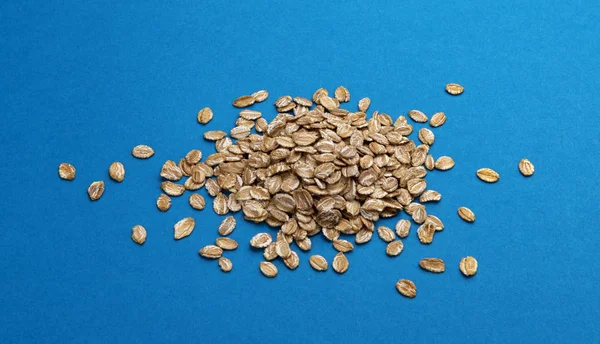 Heap of rye flakes on blue color background, top view