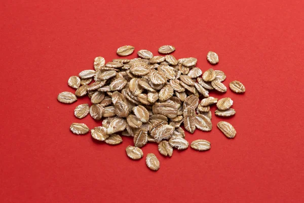 Pile of oat rye flakes on red color background — Stock Photo, Image