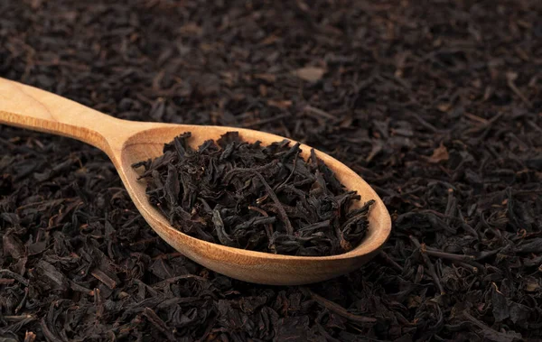 Hojas de té secas en cuchara de madera aisladas sobre fondo oscuro — Foto de Stock