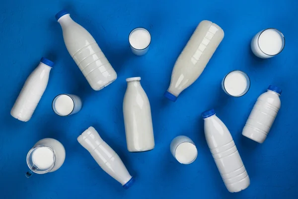 Embalaje de productos lácteos, botellas y vasos con leche sobre fondo azul, vista superior — Foto de Stock