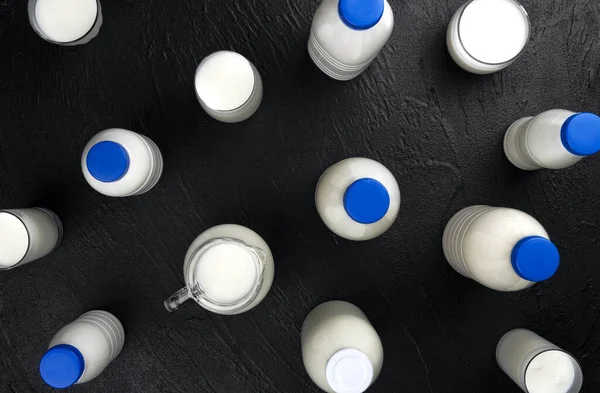 Zuivelproducten verpakking, flessen en glazen met melk op zwarte achtergrond, bovenaanzicht — Stockfoto