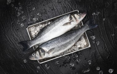 Seabass fish on metal tray on black stone background