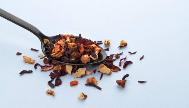 Beyaz arka planda kaşık içinde meyve çayı yaprakları