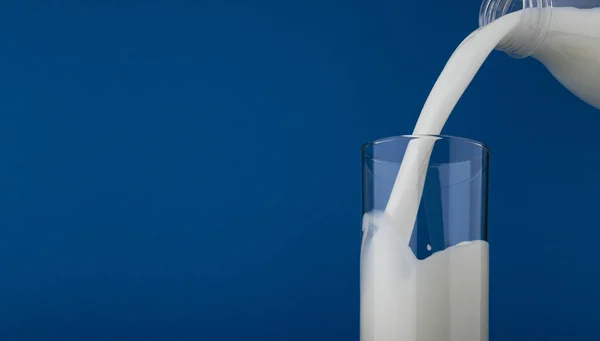 Milch in Glas einschenken isoliert auf blauem Hintergrund — Stockfoto