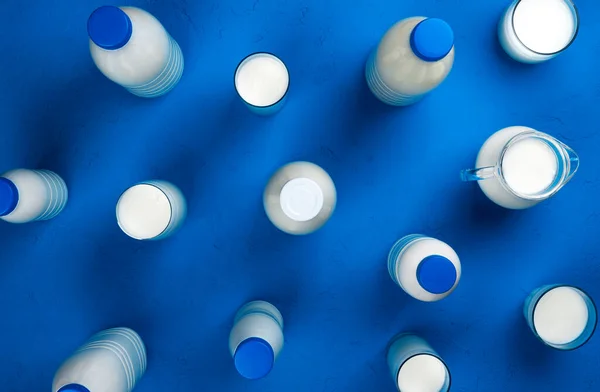 Colección de botellas y vasos con leche sobre fondo azul, vista superior — Foto de Stock