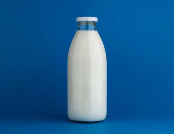 Skleněná láhev mléka napodobit na modrém pozadí — Stock fotografie