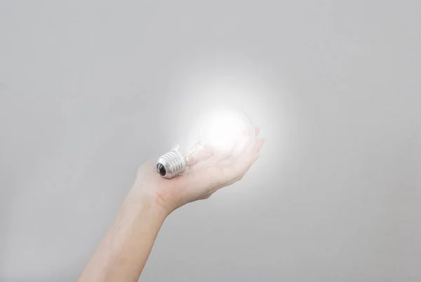 La mano de la mujer sostiene una bombilla eléctrica incandescente que brilla. Cr. — Foto de Stock