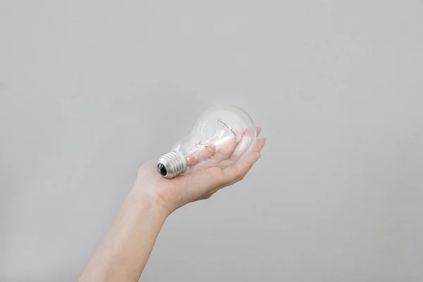La mano de la mujer sostiene una bombilla eléctrica de incandescencia. Creación de un — Foto de Stock