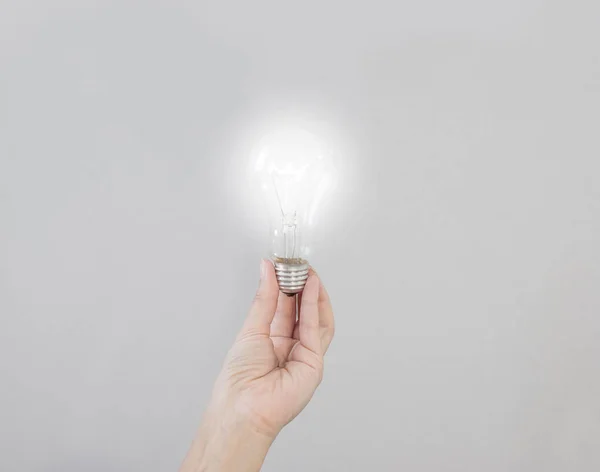 La mano de la mujer sostiene una bombilla eléctrica incandescente que brilla. Cr. — Foto de Stock