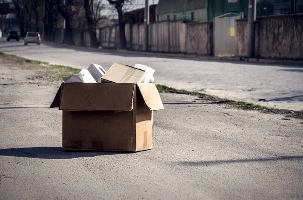 Kartonnen doos met kantoorbenodigdheden op de weg op het asfalt. Ontslag van het werk, uitzetting van het appartement — Stockfoto