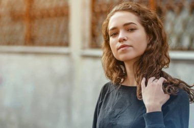 Terk edilmiş sanayi binasının arka planında siyah ceketli kıvırcık saçlı hoş bir kız portresi. Yüzü yakın çekim.