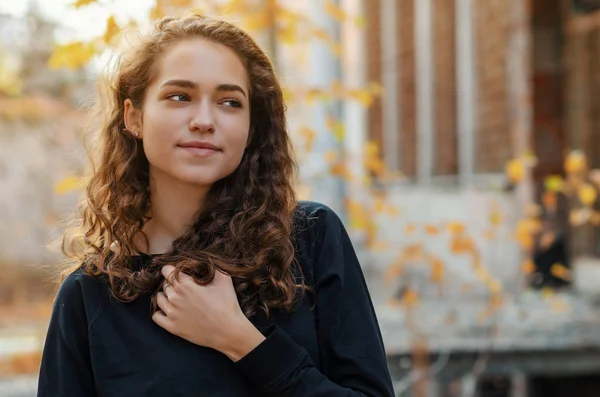 Retrato de menina agradável com cabelo encaracolado em casaco escuro no edifício de fundo amarelo. Face close-up . — Fotografia de Stock