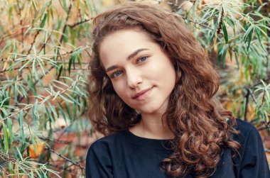 Yeşil çalılık deniz dikenli arka planda kahverengi kıvırcık saçlı bir kızın portresi..