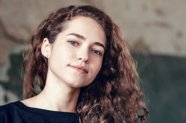 Güzel kız, boyalı duvarın arka planında pastel renkte bir portre. Yüzünde mükemmel bir gülümseme, kıvırcık saçlı. Yakın plan..