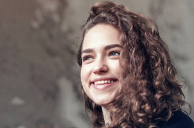 Güzel kız, boyalı duvarın arka planında pastel renkte bir portre. Yüzünde mükemmel bir gülümseme, kıvırcık saçlı. Yakın plan..