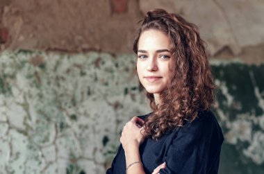 Güzel kız, boyalı duvarın arka planında pastel renkte bir portre. Yüzünde mükemmel bir gülümseme, kıvırcık saçlı. Yakın plan..