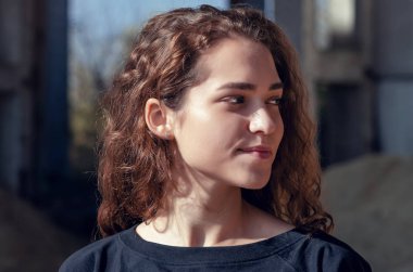 Güneş altında kıvırcık saçlı güzel bir kızın yakın plan portresi endüstriyel alanda beton bir binada uçuyor..