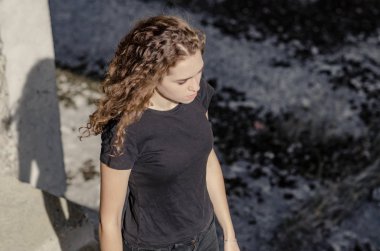 Uzun kıvırcık saçlı hoş bir kız. Üst manzara, sanayi bölgesi boyunca uzanıyor, beton bina..