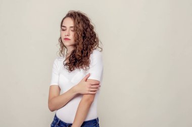 Güzel üzgün kız açık sarı arka planda duruyor, aşağı bakıyor..