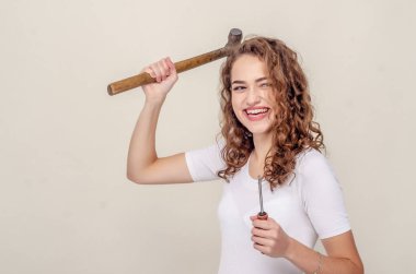Genç kıvırcık, neşeli kız beceriksizce elinde tornavida ve çekiç tutuyor.