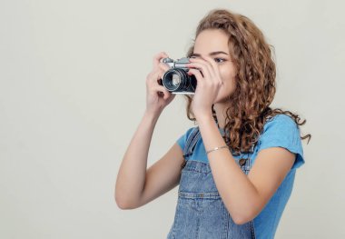 Kot pantolon giyen kıvırcık esmer kız elinde klasik bir film kamerası tutuyor. Bir fotoğraf çekiyor. Yan görünüm.