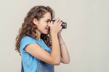 Kot pantolon giyen kıvırcık esmer kız elinde klasik bir film kamerası tutuyor. Bir fotoğraf çekiyor. Yan görünüm.