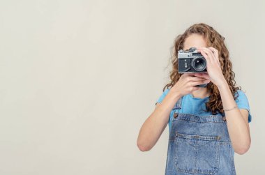Kot pantolon giyen kıvırcık esmer kız elinde klasik bir film kamerası tutuyor. Fotoğraf çeker.