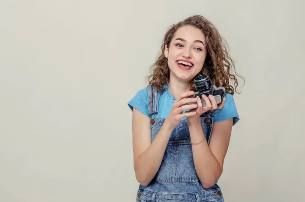 Curly brune joyeuse en salopette en denim tient une caméra de film en — Photo