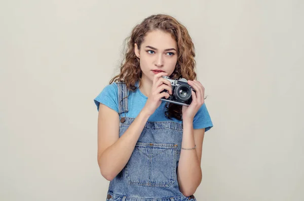 Ricci bruna allegra in tuta di jeans tiene una macchina fotografica tra le mani, divertendosi sul set . — Foto Stock