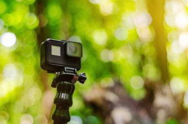 Yeşil orman arka planında esnek bir üçayak üzerinde aksiyon kamerası