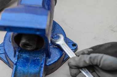 İşçi eli mavi metal mengenenin vidalarını söküyor.
