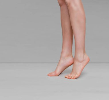 İnce kadın bacakları açık gri arka planda parmak uçlarında yükseliyor.