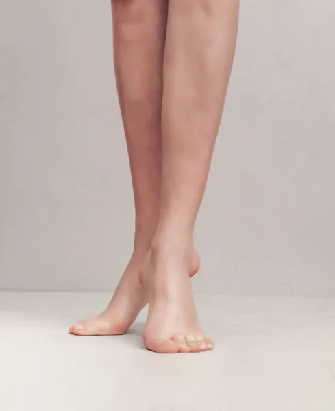 Gambe femminili snelle sollevate sulle dita dei piedi su uno sfondo grigio chiaro — Foto Stock