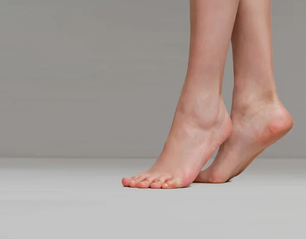 Delgadas piernas femeninas levantadas en los dedos de los pies sobre un fondo gris claro — Foto de Stock