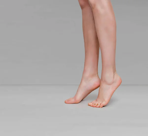 Delgadas piernas femeninas levantadas en los dedos de los pies sobre un fondo gris claro —  Fotos de Stock