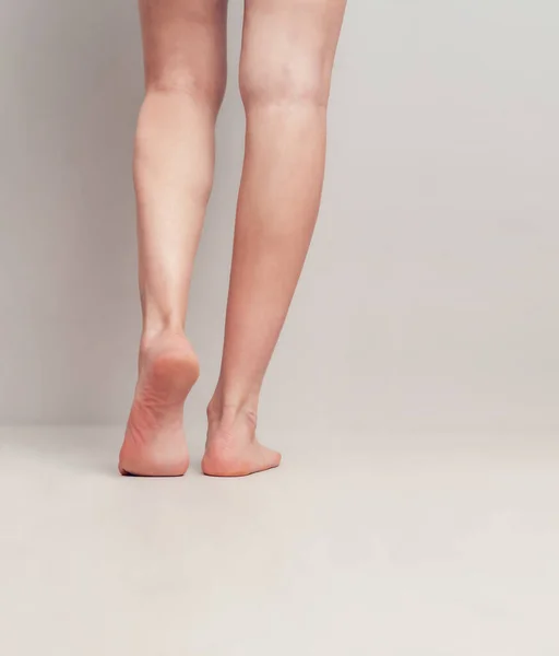 Slender female legs raised on toes on a light gray background