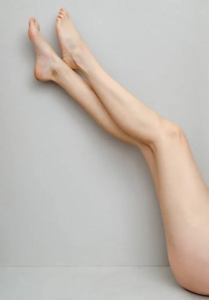 Slender legs of a woman bent to her knees on a gray background — Stock Photo, Image