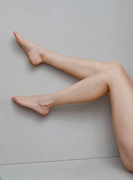 Patas delgadas de una mujer doblada de rodillas sobre un fondo gris —  Fotos de Stock