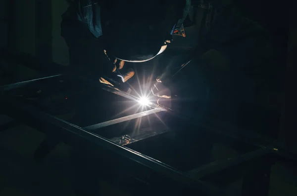 Welding a metal product in metal workshop. Bright glow of an electric arc. Fabrication of metal mounts