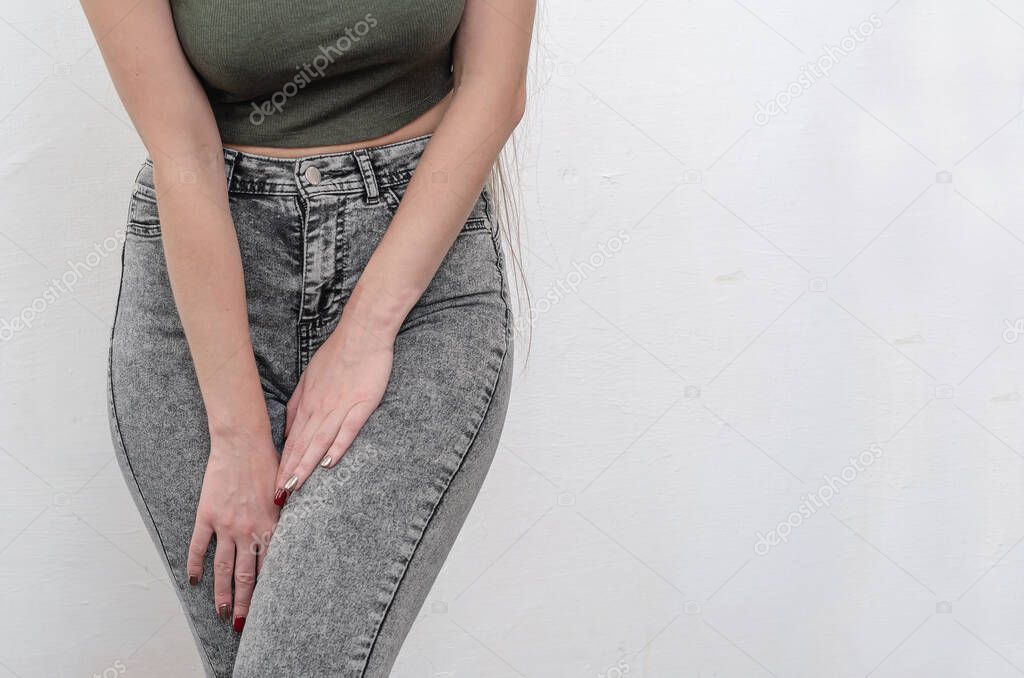 Young slim girl in jeans holds hands pressed between her legs. Women's health, gynecology