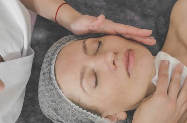 Spa salonundaki kanepede kozmetik şapkalı bir kadın. Kozmetik işlemler için yüz derisinin hazırlanması, temizlik, masaj, rahatlama