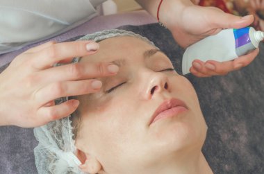 Spa salonundaki kanepede kozmetik şapkalı bir kadın. Kozmetik işlemler için yüz derisinin hazırlanması, temizlik, masaj, rahatlama