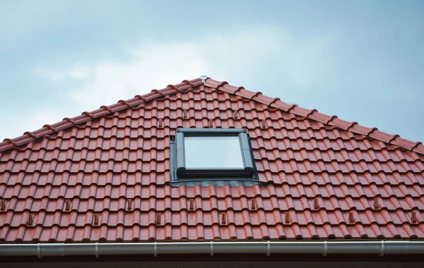 Close up on house roof window, sun tunnel skylights or skylight after rain on red ceramic clay tiles roof. Attic skylight solution outdoor. Roofing Construction.