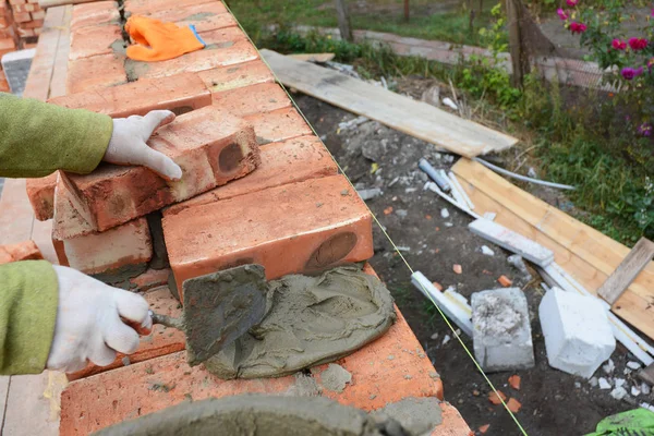 Bricklaying. Bricklayer worker installing red blocks and caulking brick masonry joints exterior brick house  wall with trowel putty knife outdoor.