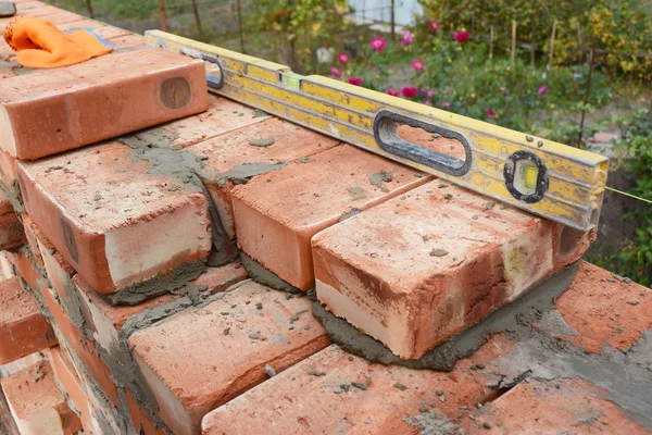 Murning med vattenpass att kontrollera nya rött tegel husvägg utomhus. Grundläggande bricklayingen. — Stockfoto