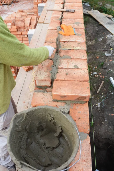 Bricklaying, Brickwork.Bricklayer worker installing red blocks and caulking brick masonry joints exterior brick house wall with trowel putty knife outdoor.