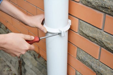 İşçi yükleme yağmur oluk downpipe. Yüklenici eller onarım yağmur oluk downspout boru tornavida ile. Yaşamadönüşmesi, dereleri, yaşamadönüşmesi, eriyip plastik ve drenaj. Guttering aşağı boru bağlantı parçaları